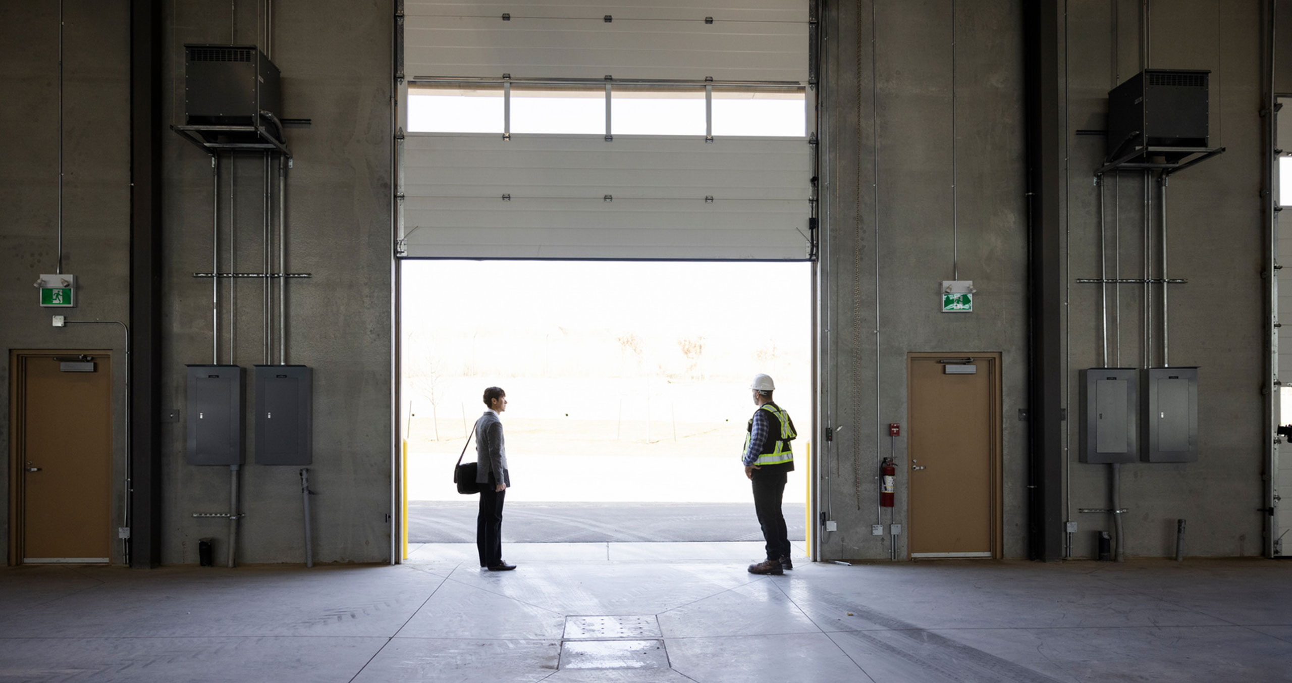 Two men are talking in the hall door. One has a suit on and the other an overalls.